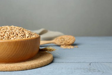 Açık mavi ahşap masada buğday taneleriyle dolu bir kâse. Metin için boşluk