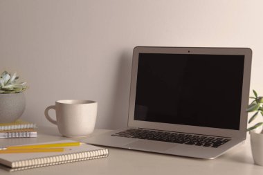 Modern dizüstü bilgisayar kupası ve defterler beyaz masada.