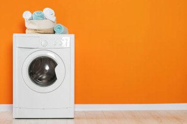 Turuncu duvarın yanında temiz havluları olan çamaşır makinesi, mesaj için yer. İç tasarım
