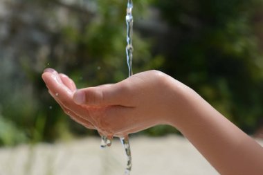 Pouring water into kid`s hand outdoors, closeup