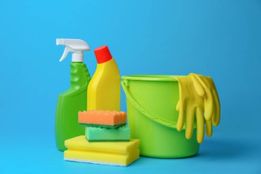 Green bucket, cleaning supplies and tools on light blue background