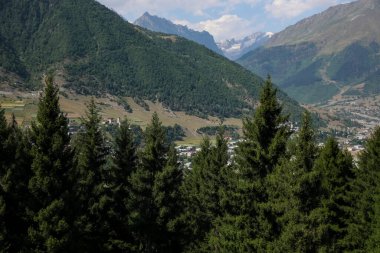 Açık mavi bulutlu gökyüzünün altında güzel ağaçlar ve dağlar
