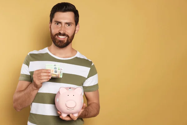 Happy Man Putting Money Piggy Bank Beige Background Space Text — Stock Photo, Image