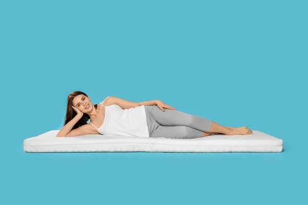 Genç Bir Kadın Açık Mavi Arka Planda Yumuşak Bir Yatakta — Stok fotoğraf