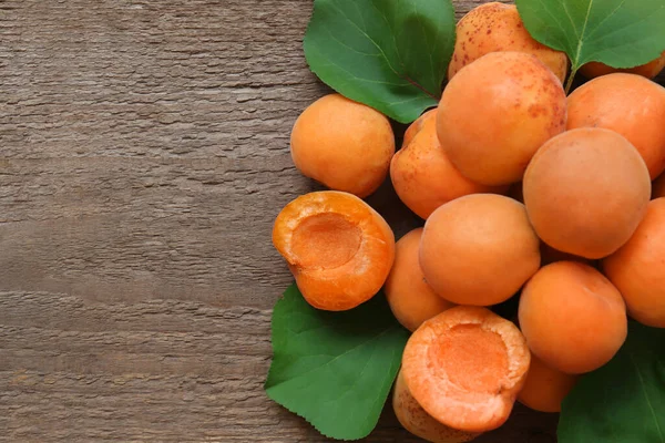 stock image Delicious ripe apricots with green leaves on wooden table, top view. Space for text