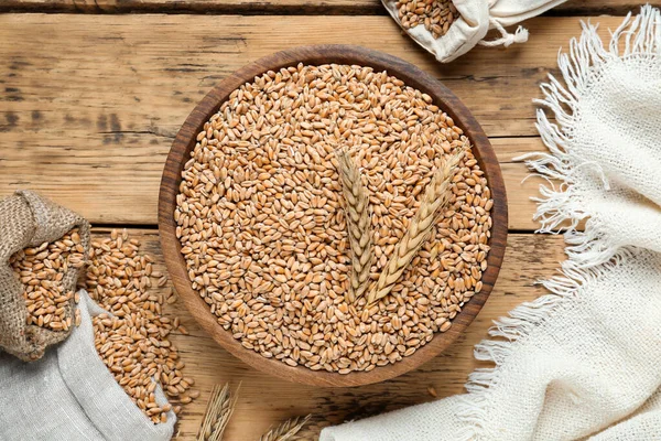 stock image Bowl of wheat grains and spikes on wooden table, flat lay