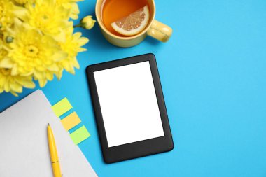 Defteri olan bir e-kitap okuyucusu, açık mavi arka planda bir fincan çay ve çiçekler, düz uzanmış. Metin için boşluk