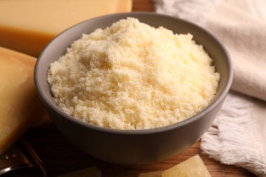 Delicious grated parmesan cheese in bowl on wooden table, closeup