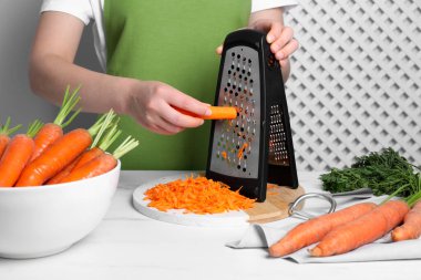 Woman grating fresh carrot at table indoors, closeup clipart