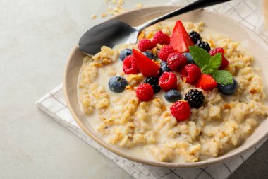 Bowl of oatmeal porridge served with berries on light grey table, closeup