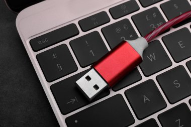 Koyu masada kırmızı USB kablo ve dizüstü bilgisayar, yakın plan.