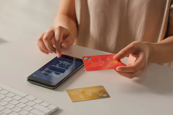 stock image Woman using online banking app on smartphone and credit card at white office table, closeup