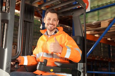 Depodaki forklift kamyonunda oturan mutlu işçi.