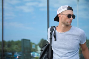 Güneş gözlüklü ve sırt çantalı yakışıklı genç adam yansıma yüzeyinin yanında, metin için yer var.