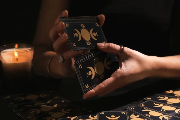 Soothsayer shuffling tarot cards at table in darkness. Fortune telling