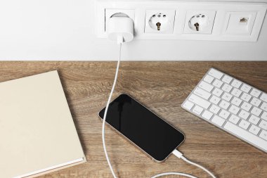 Modern akıllı telefon ahşap masada şarj oluyor.