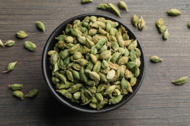 Bowl of dry cardamom pods on wooden table, top view