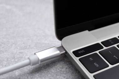 C tipi konnektörü olan USB kablosu gri masadaki laptop portuna takılı, yakın plan
