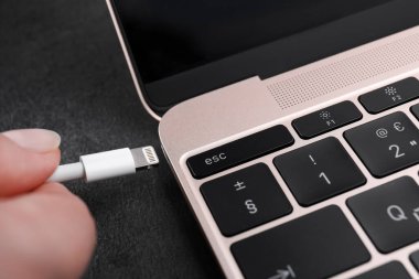 Karanlık masadaki laptop portuna USB kablosunu yıldırım konnektörüyle bağlayan kadın.