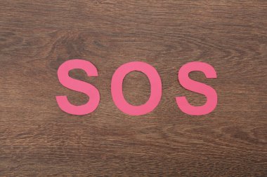 Ahşap zemin üzerinde kağıt harflerden oluşan kısaltma SOS, üst görünüm