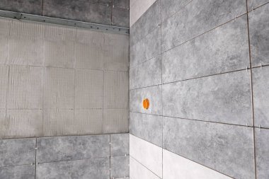 Gri modern fayanslı duvarlar, yapıştırıcı karışımı ve elektrik prizleri için hazırlanmış delik.