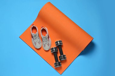 Egzersiz paspası, halterler ve ayakkabılar turkuaz arka planda, düz yatış