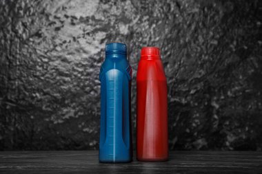 Kara duvarın yanındaki siyah masada farklı kaplarda motor yağı var.