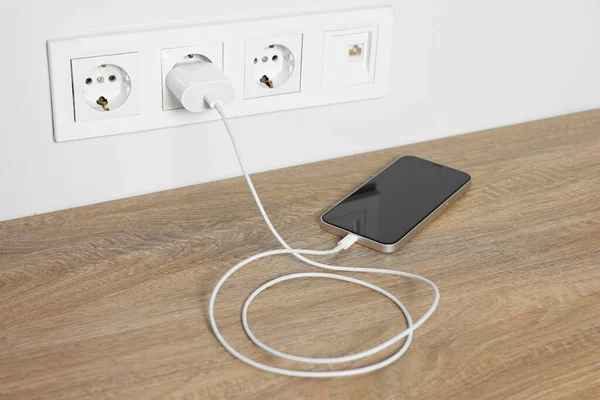 stock image Modern mobile phone charging on wooden table