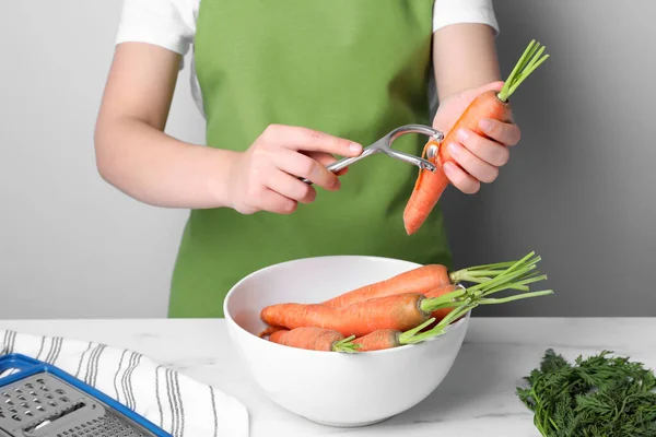 Woman peeling fresh carrot at white table indoors