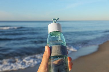 Woman holding glass bottle with water near sea, closeup clipart