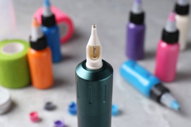 Profesyonel dövme makinesi ve açık gri masa üzerindeki mürekkepler, yakın plan.