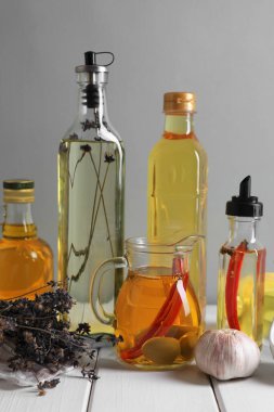 Gri arka planda beyaz ahşap masada farklı yağlar ve malzemeler var.