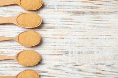 Kahverengi granüle şekerli kaşıklar açık ahşap masada, düz yatıyordu. Metin için boşluk