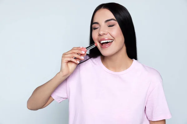 stock image Young woman with beautiful makeup holding nude lipstick on light gray background