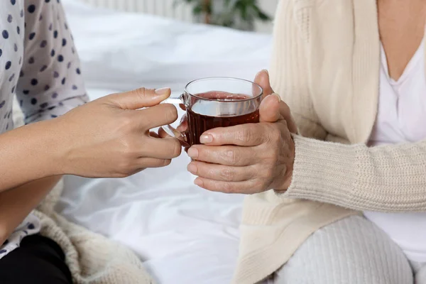 stock image Caregiver giving tea to elderly woman at home, closeup