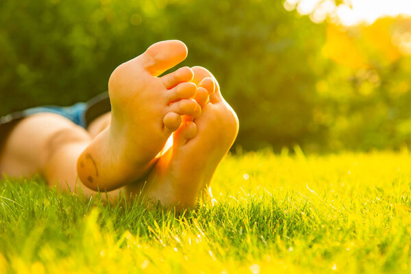 Teenage girl lying barefoot on green grass outdoors, closeup. Space for text