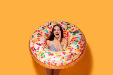 Turuncu arka planda şişme yüzük takan genç bir kadın.