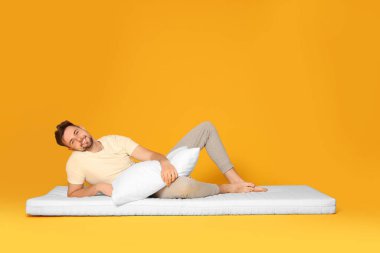 Turuncu arka planda yumuşak yatakta poz veren gülümseyen adam.