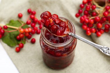 Spoon and jar with tasty viburnum jam on table clipart