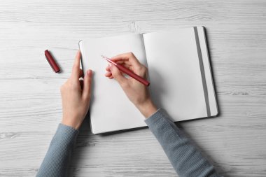 Woman writing in notebook at white wooden table, top view clipart