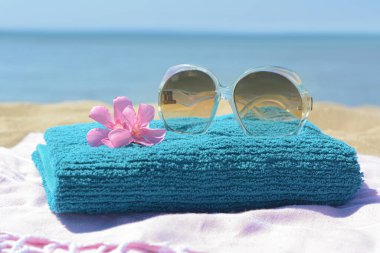 Havlulu battaniye, deniz kenarında şık güneş gözlükleri ve çiçekler, yakın plan. Plaj aksesuarları
