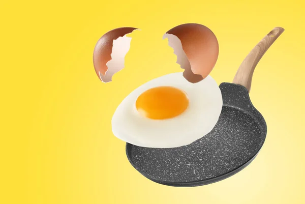 Tasty fried chicken egg with shell falling into frying pan on yellow background