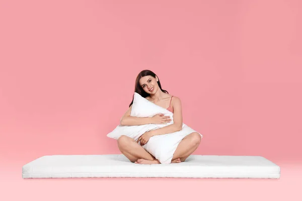 软垫上的年轻女子抱着枕头 衬托着苍白的粉色背景 — 图库照片