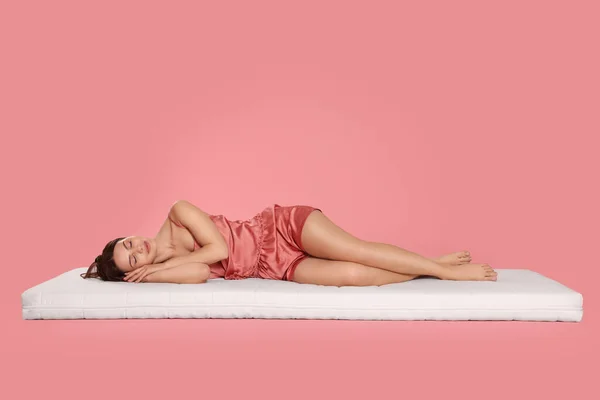 若いです女性寝ています上の柔らかいマットレスに対して淡いピンクの背景 — ストック写真