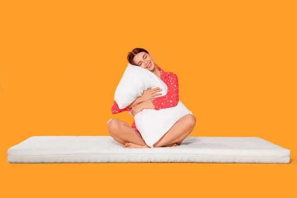 坐在软垫上抱着枕头的年轻女子 衬托着橙色背景 — 图库照片