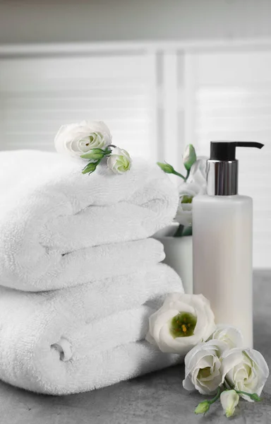 Cosmetic product, folded towels and flowers on gray marble table