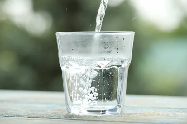 Pouring pure water into glass on light blue wooden table against blurred background