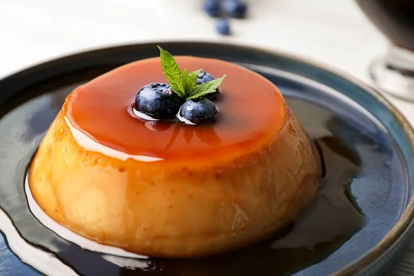 stock image Plate of delicious caramel pudding with blueberries and mint on table, closeup