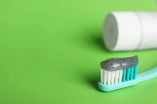 Brush with charcoal toothpaste on green background, closeup. Space for text