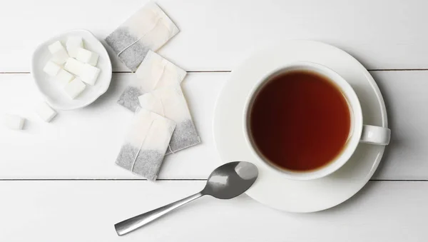 stock image Tea bags and sugar near cup of hot drink on white wooden table, flat lay